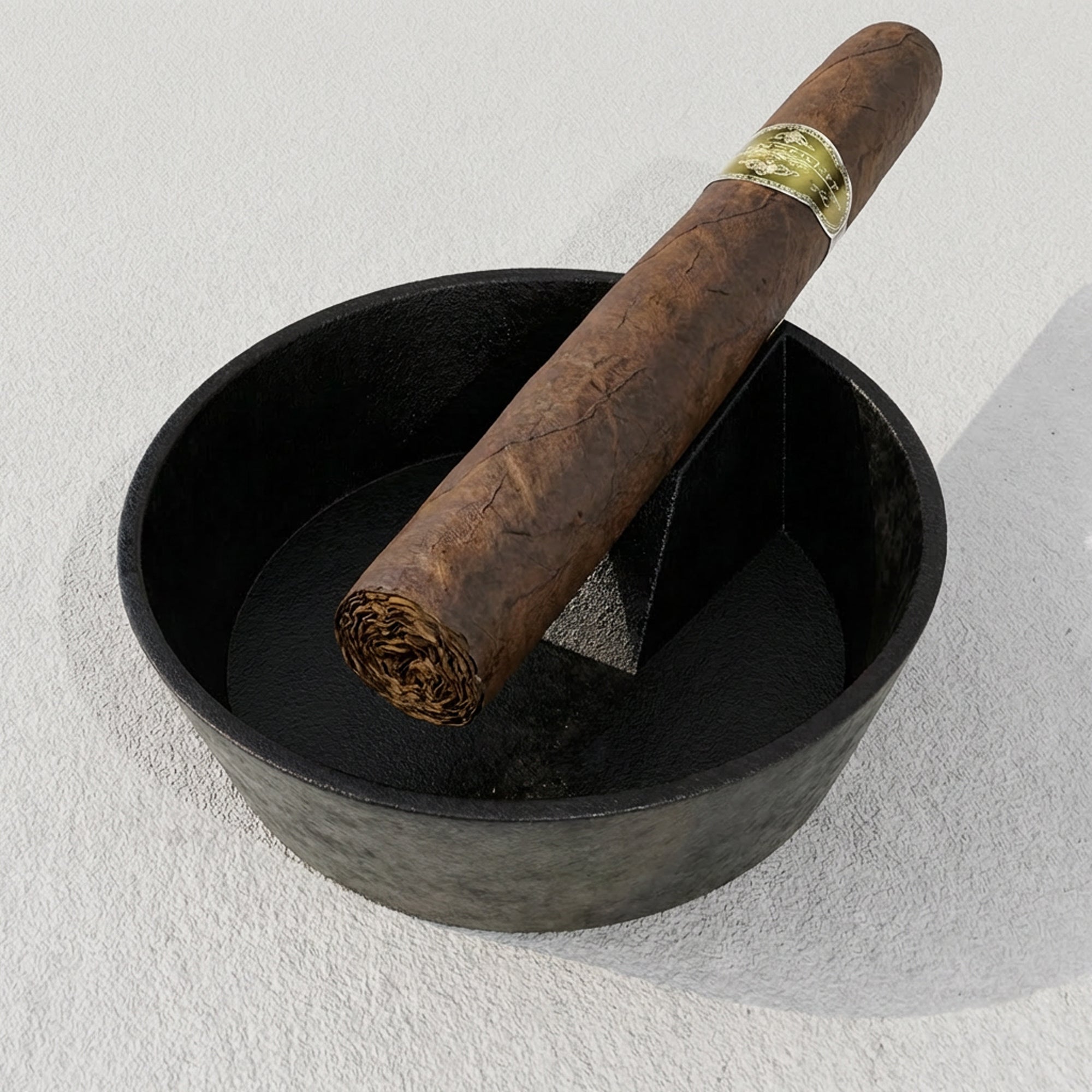 Cigar with a gold band in a black bowl on a light gray background