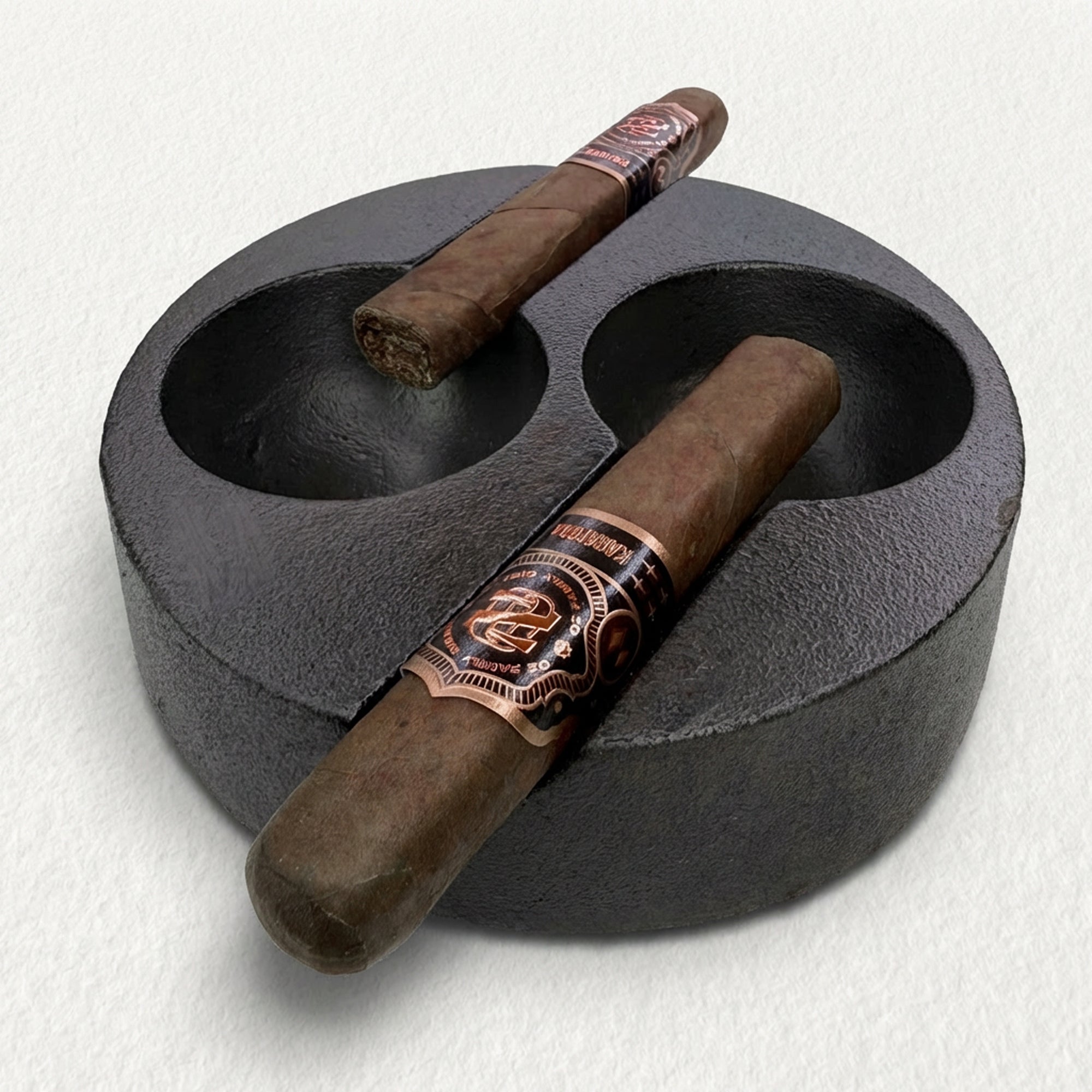 Two cigars with decorative bands in a casy iron ashtray on a light gray background
